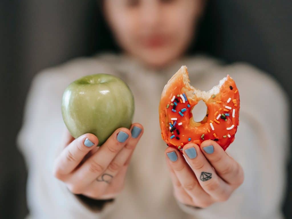 Adolescente muestra una manzana, propia de ambiente saludable, y un donuts, de ambiente obesogénico