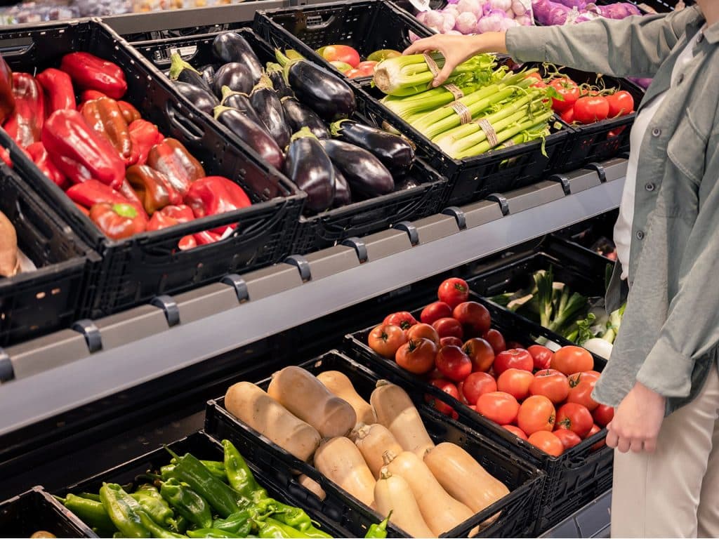 Persona eligiendo verduras frescas en supermercado.