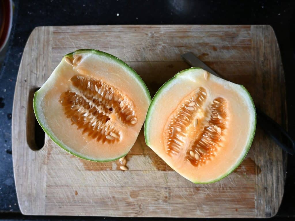 Mel&oacute;n partido por la mitad, fruta fresca e hidratante sobre una tabla de madera
