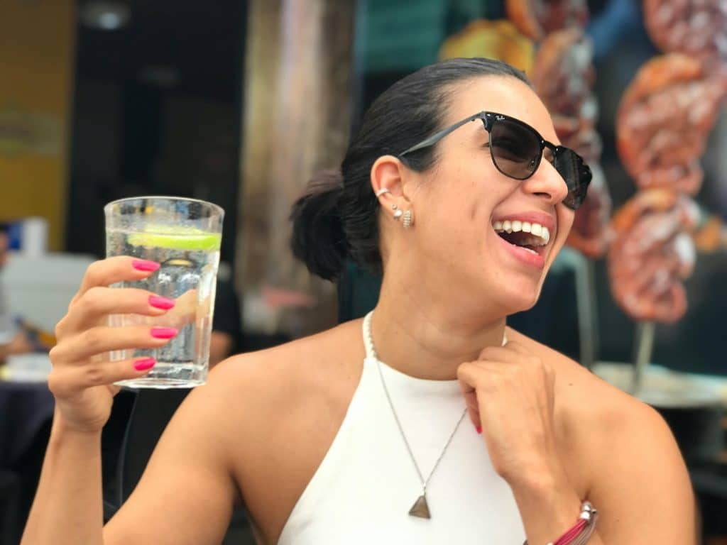 Mujer sonrie con un vaso de agua en la mano mientras esta en una terraza