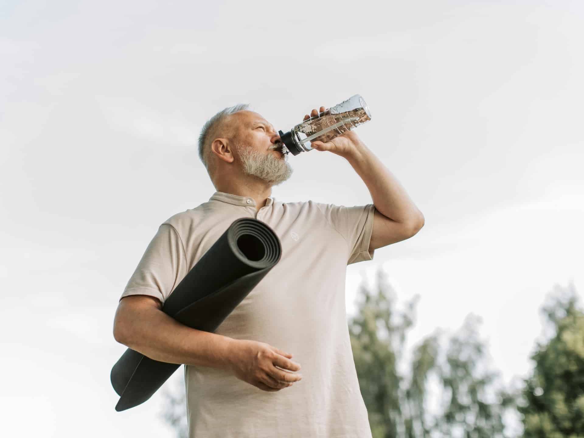 Hombre bebiendo agua con una esterilla de yoga