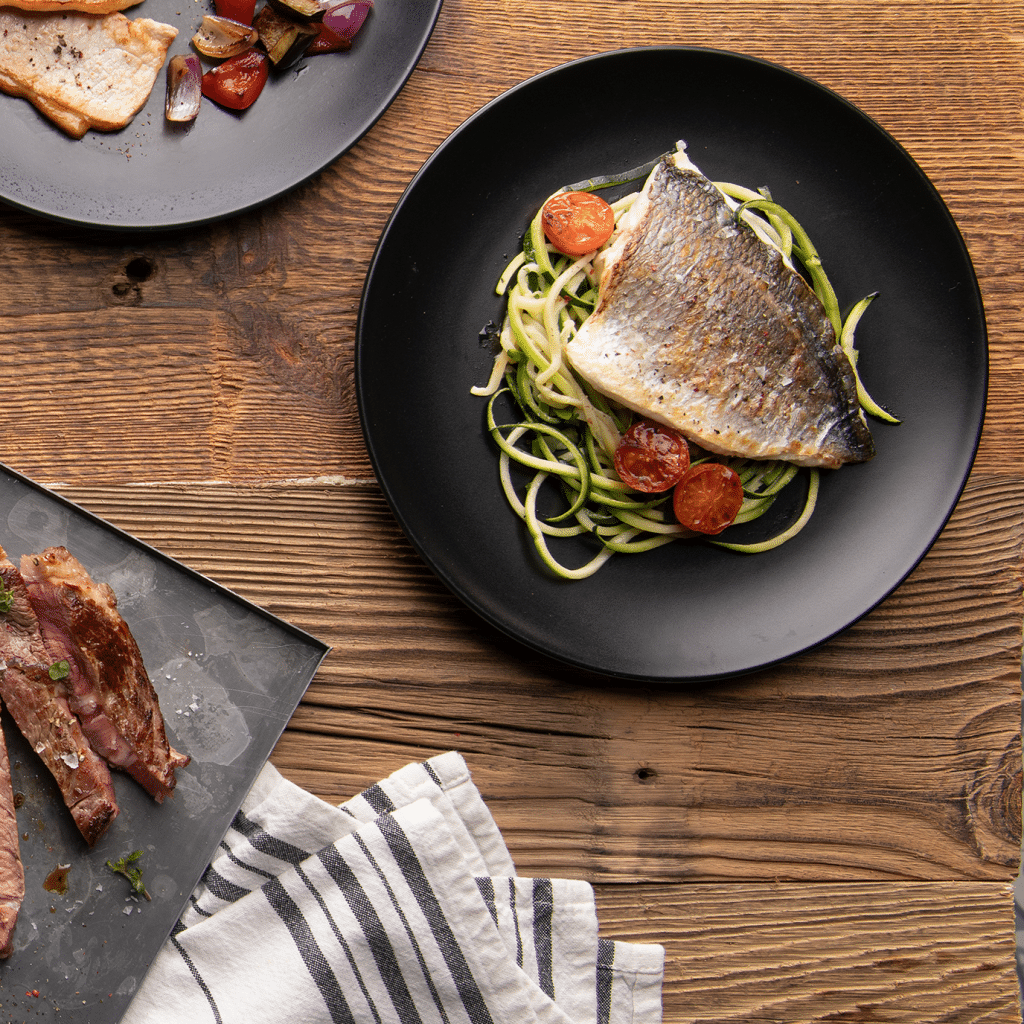 Plato sobre una mesa de cocina con alimentos con col&aacute;geno y f&aacute;ciles de incluir en el d&iacute;a a d&iacute;a: pollo con piel, salm&oacute;n con piel, gelatina neutra y c&iacute;tricos.