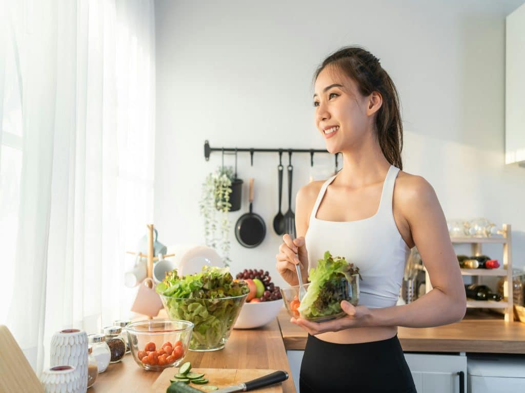 Mujer joven sonriente en una cocina luminosa sosteniendo un bol de ensalada fresca.
