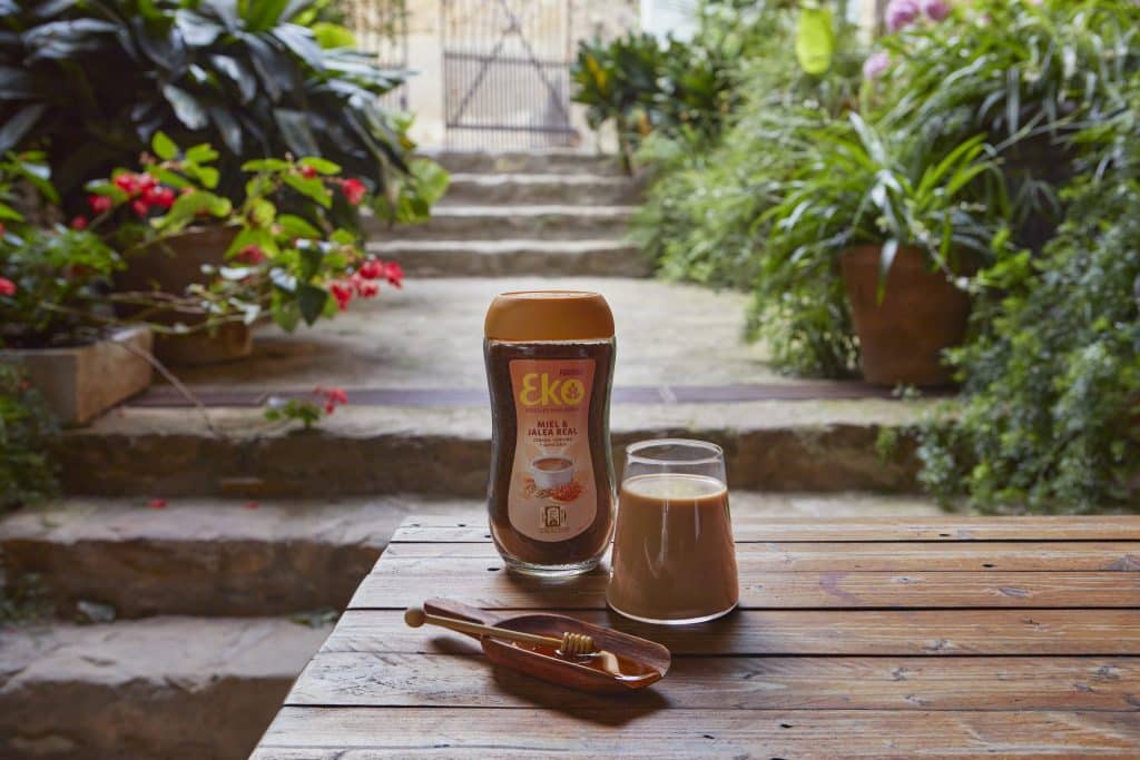 Bote de EKO Miel y Jalea Real en una mesa de madera exterior con un vaso preparado y miel natural.