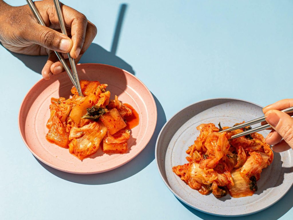 Dos platos con kimchi coreano tradicional fermentado servido con palillos sobre un fondo azul brillante.