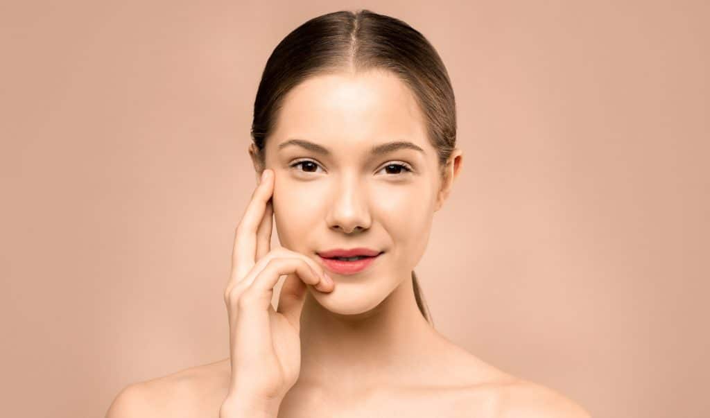 Primer plano de una mujer joven con piel saludable toc&aacute;ndose el rostro suavemente