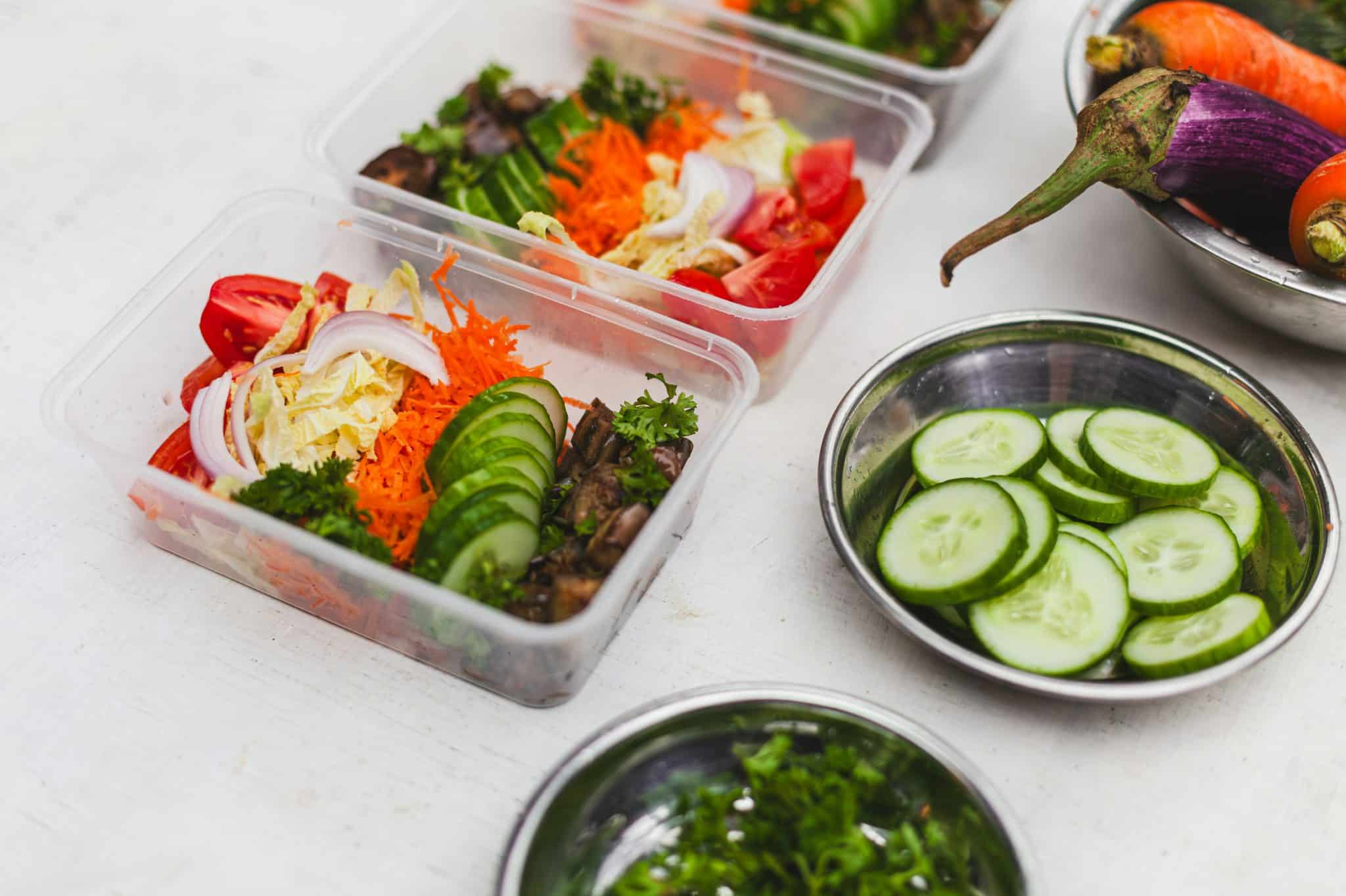 Varios táperes de plástico transparente con ensaladas preparadas que llevan pepino, zanahoria rallada, tomate y cebolla, listos para llevar al trabajo.